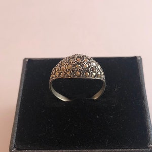 May include: A silver ring with a domed top set with small, dark grey stones. The ring is displayed in a black velvet box.