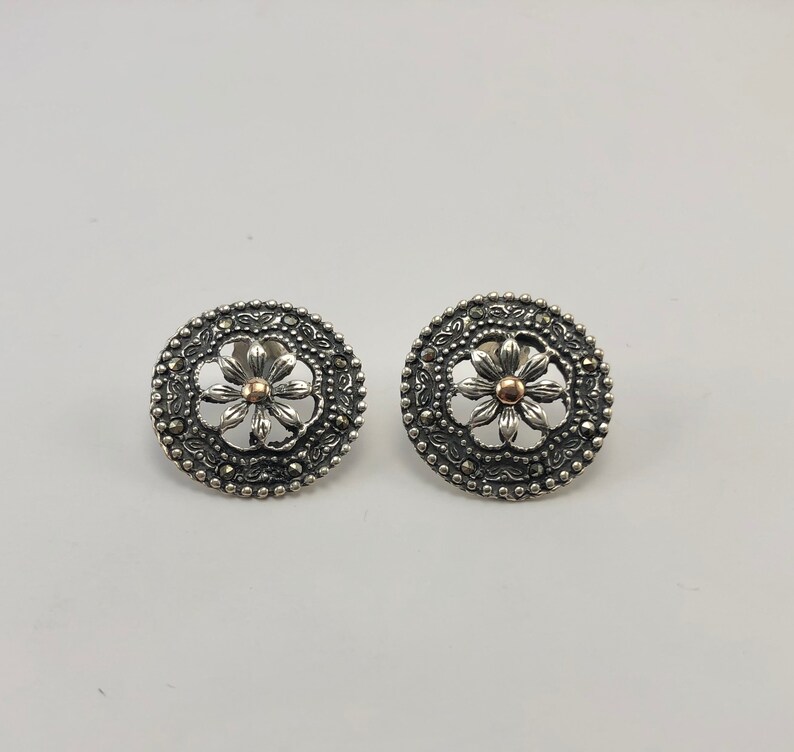May include: A pair of silver earrings with a floral design. The center of each earring features a small, round, rose gold accent.