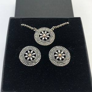May include: A silver necklace and earrings set with a delicate floral design. The pendant and earrings feature a silver flower with a gold center.