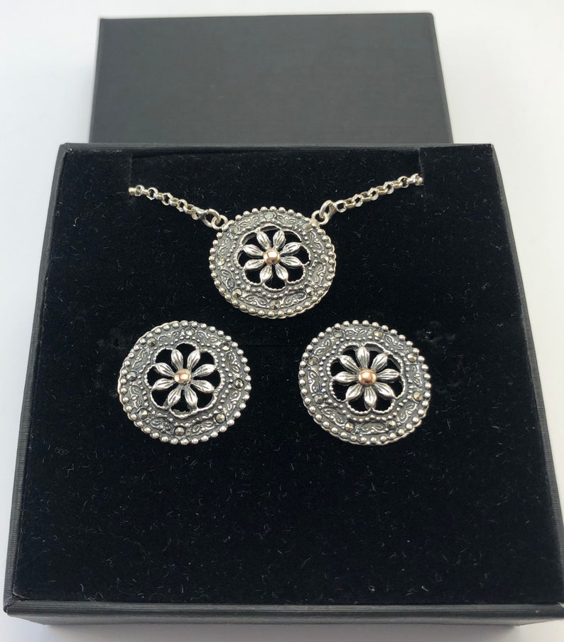 May include: A silver necklace and earrings set with a delicate floral design. The pendant and earrings feature a silver flower with a gold center.