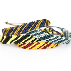 May include: Four friendship bracelets with different color combinations. The bracelets are made with woven string in yellow, red, black, white, blue, and green.