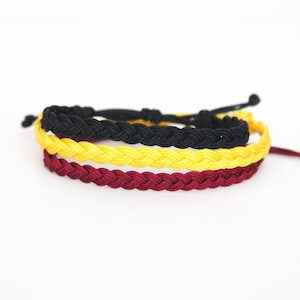 May include: Three braided friendship bracelets in black, yellow, and burgundy.