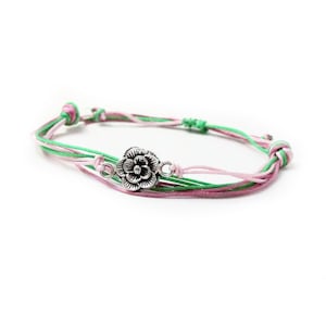 May include: A green and pink friendship bracelet with a silver flower charm.