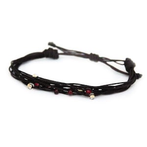 May include: A brown braided bracelet with red and silver beads.