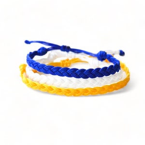May include: Three braided friendship bracelets in yellow, white, and blue.