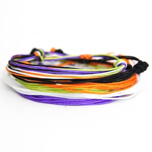 May include: A stack of colorful bracelets in purple, white, green, orange, and black. The bracelets are made of thin cord and are tied together in a knot.