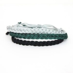 May include: Three braided bracelets in black, dark green, and light gray.