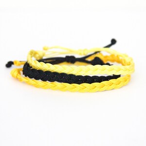 May include: Two braided friendship bracelets, one black and one yellow.