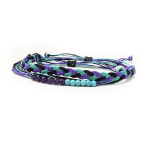 May include: A braided friendship bracelet with purple, teal, and black threads. The bracelet has a row of purple and teal beads.