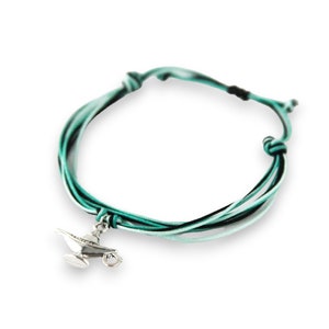 May include: A green, black, and white braided cord bracelet with a silver charm of a genie lamp.