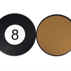 May include: A black and white 8-ball coaster with a cork backing. The coaster is round and has a black border.