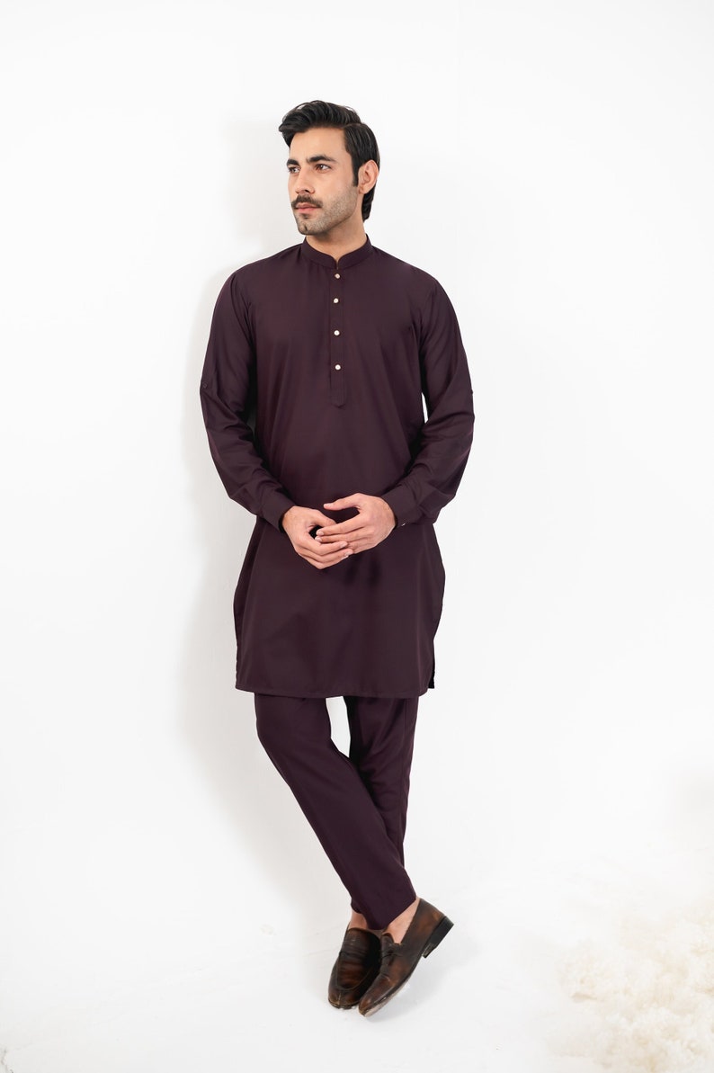 May include: A man wearing a long-sleeved, dark purple kurta with a button-up collar and matching pants. He is wearing brown leather loafers.