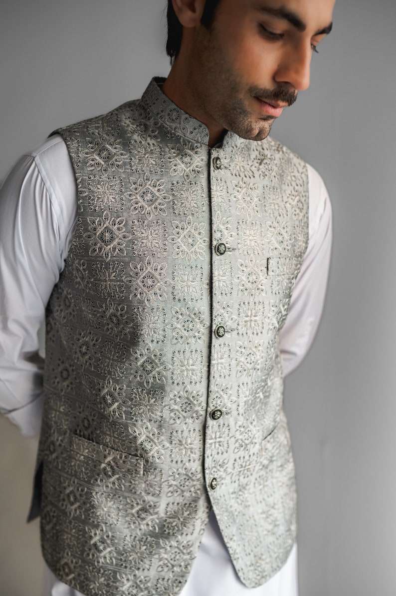 May include: A gray waistcoat with a white embroidered pattern. The waistcoat has a mandarin collar and a button closure.
