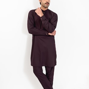 May include: A man wearing a long-sleeved, dark purple kurta with matching pants and brown leather shoes. He is standing with his arms crossed and looking to the side.