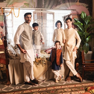 May include: Five people, including three children, are standing in a room with a bed, a chair, and a table. They are all wearing traditional clothing. The room is decorated with colorful murals and patterned tiles.