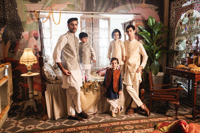 May include: Five people, including three children, are standing in a room with a bed, a chair, and a table. They are all wearing traditional clothing. The room is decorated with colorful murals and patterned tiles.