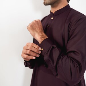 May include: A burgundy long-sleeved shirt with a mandarin collar and gold buttons. The shirt is made of a smooth, wrinkle-resistant fabric.