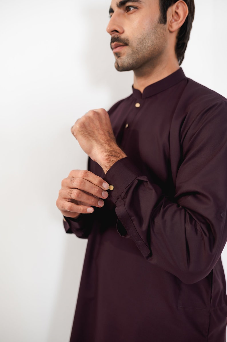 May include: A burgundy long-sleeved shirt with a mandarin collar and gold buttons. The shirt is made of a smooth, wrinkle-resistant fabric.