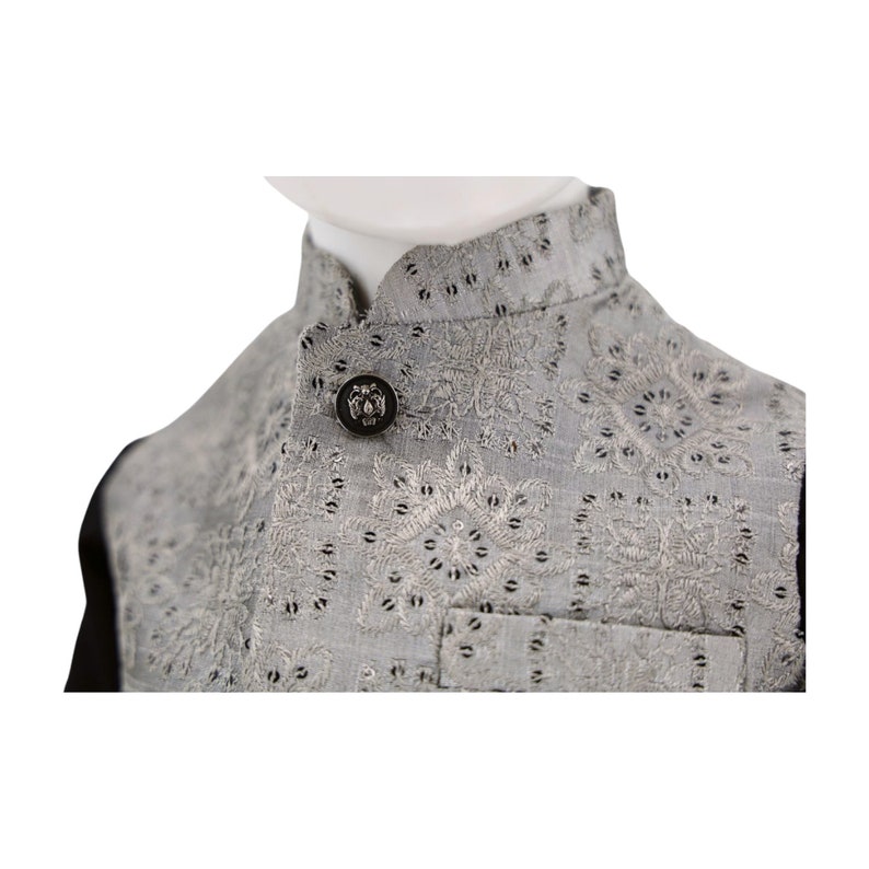 May include: A gray vest with a silver button and intricate embroidery. The vest has a mandarin collar and a black lining.