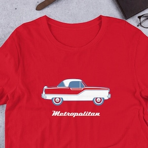 Può includere: Maglietta rossa a maniche corte con un'illustrazione di un'auto bianca e rossa e il testo "Metropolitan" stampato sul davanti.