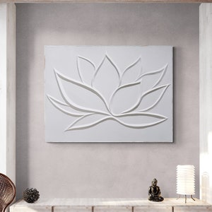 May include: White wall art with a raised, embossed design of a lotus flower. The art is framed and hanging on a white wall.