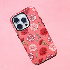 May include: A phone case with a floral pattern of red and pink carnations and green leaves on a coral background. The case has a black border and a camera cutout.