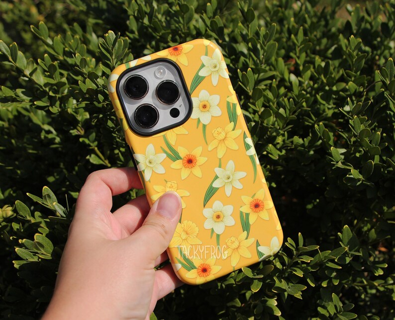 May include: Yellow phone case with a floral daffodil pattern. The case features white, yellow, and orange flowers with green leaves. The brand name "TACKYFROG" is printed on the bottom of the case.