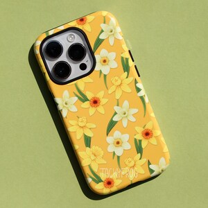 May include: Yellow phone case with a floral pattern of white and yellow daffodils and green leaves. The case has a black camera lens area and the text "TACKYFROG" at the bottom.