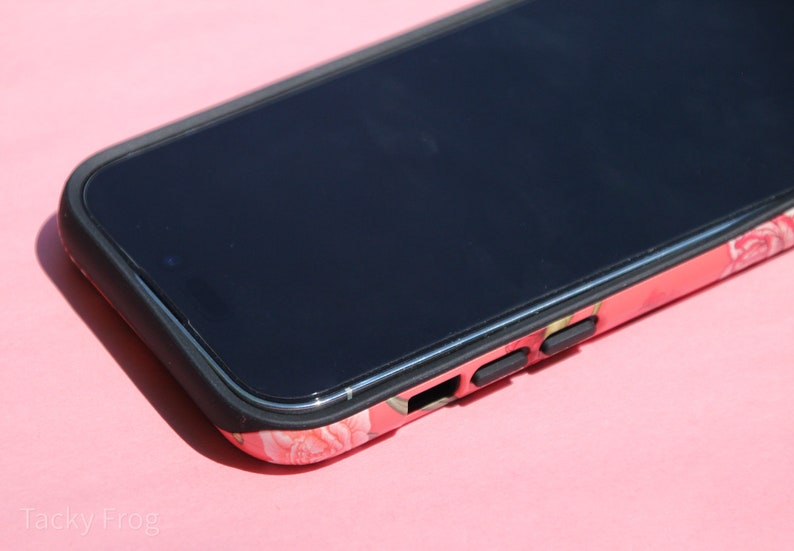 May include: A smartphone in a floral print case with a black border. The case features a pattern of pink and white flowers. The phone's screen is black, and the case has black buttons on the side.