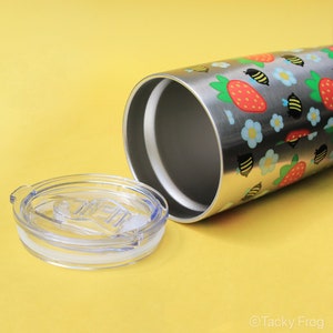 Puede incluir: Vaso de acero inoxidable con tapa transparente. El vaso est&aacute; decorado con un estampado de fresas, abejas y flores azules. La tapa es transparente con una junta blanca.