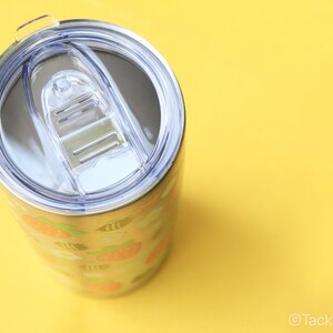 Puede incluir: Vaso de acero inoxidable con tapa de pl&aacute;stico transparente. El vaso presenta un patr&oacute;n repetido de fresas naranjas, hojas verdes y abejas amarillas. El vaso est&aacute; sobre un fondo amarillo brillante.