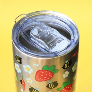 Puede incluir: Vaso de acero inoxidable con tapa de pl&aacute;stico transparente. El vaso est&aacute; decorado con ilustraciones coloridas de fresas, abejas y flores. La tapa tiene un cierre deslizante.
