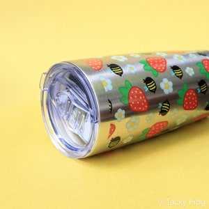 Puede incluir: Vaso de acero inoxidable con tapa transparente. El vaso est&aacute; decorado con un estampado de fresas rojas, abejas amarillas y negras y flores blancas y azules. El vaso es cil&iacute;ndrico y tiene un acabado plateado.
