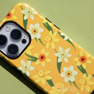 May include: Yellow phone case with a floral pattern of daffodils. The case features a repeating design of yellow and white flowers with green leaves. The phone's camera lenses are visible.