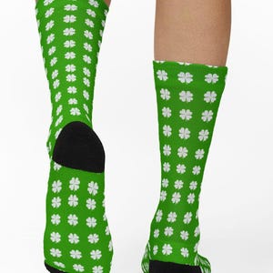 Puede incluir: Calcetines verdes con un estampado de tréboles blancos de cuatro hojas. Los calcetines tienen talones y punteras negras. Los calcetines son hasta la rodilla y los lleva una persona.