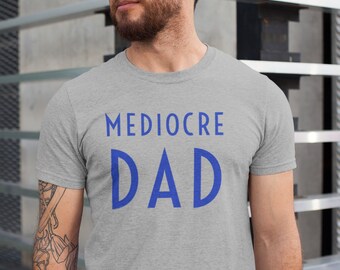 Puede incluir: Una camiseta gris jaspeada con el texto "Mediocre Dad" impreso en azul.