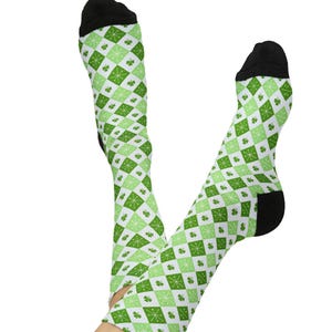 Puede incluir: Un par de calcetines hasta la rodilla con un patrón de diamantes blancos y verdes. El diseño incluye tréboles verdes y explosiones de estrellas. Los dedos de los pies y los talones son negros.