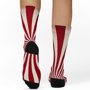 Può includere: Un paio di calzini al ginocchio con un motivo a righe rosse e bianche che si irradiano dalla caviglia. Il tallone e la punta sono neri. I calzini hanno un'estetica retrò e vintage.