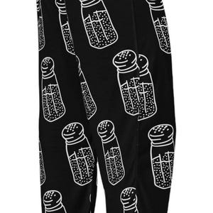 May include: Black lounge pants featuring a repeating white line art pattern of salt shakers. The shakers are depicted with a dotted texture inside to represent salt, and the pants have an elastic waistband at the top.