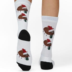 May include: White socks featuring a repeating pattern of cartoon coffee beans wearing Santa hats and holding green mugs. The socks have black heels and toes, perfect for the holiday season.