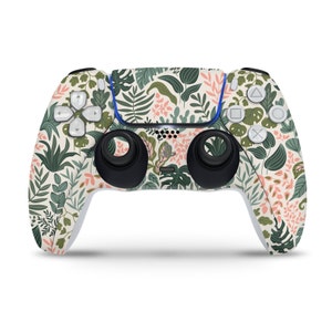 Peut inclure: Une manette de jeu PlayStation 5 DualSense blanche avec un motif floral composé de feuilles vertes et de fleurs roses.