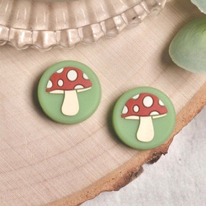 May include: Two green and white mushroom-shaped buttons with red and white spots. The buttons are round and have a raised design.