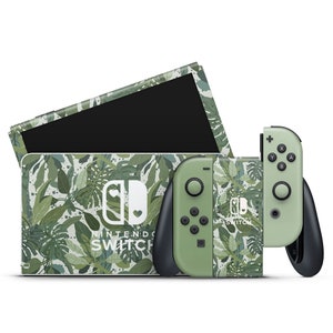 May include: A green and white Nintendo Switch console and controller with a tropical leaf pattern. The console has the Nintendo Switch logo and the words "Nintendo Switch" printed on it.