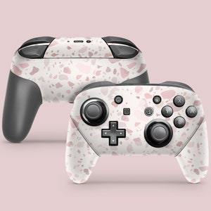 May include: A white Nintendo Switch controller with a pink and white terrazzo pattern. The controller is shown from the front and side.