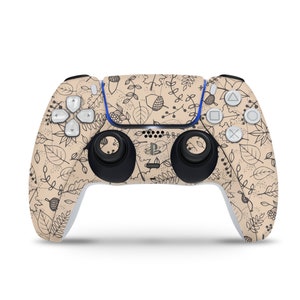 May include: A beige PlayStation 5 DualSense wireless controller with a black and white pattern of leaves, branches, and acorns. The controller has a blue and white PlayStation logo.