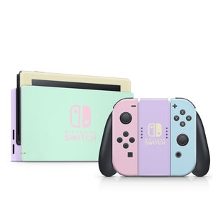 Könnte beinhalten: Eine pastellgrüne und violette Nintendo Switch Konsole mit einem passenden Paar Joy-Con Controllern. Die Konsole hat ein hellrosa Nintendo Switch Logo und die Controller haben ein hellrosa Nintendo Switch Logo auf dem rechten Controller und ein hellblaues Nintendo Switch Logo auf dem linken Controller.