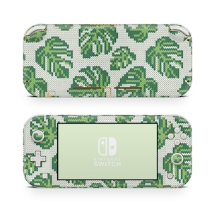 Könnte beinhalten: Eine weiße und grüne gestrickte Nintendo Switch Lite Konsole mit einem tropischen Blatt-Muster. Die Konsole hat einen grünen Knopf und einen weißen Bildschirm mit dem Nintendo Switch Logo und Text.