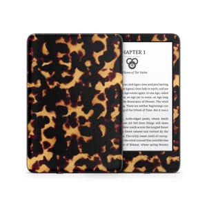 May include: A black and white e-reader with a tortoiseshell pattern cover. The screen displays the text "CHAPTER 1 Flame of Tar Valon" and a paragraph of text about the Wheel of Time.