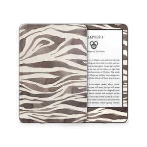 May include: A Kindle Paperwhite e-reader with a black and white zebra print cover. The screen displays the text "CHAPTER 1" and "Flame of Tar Valon".