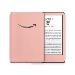 以下が含まれることがあります： 黒い縁取りのあるピンクのKindle電子書籍リーダー。画面には「CHAPTER 1」と「Flame of Tar Valon」のテキストが表示されています。